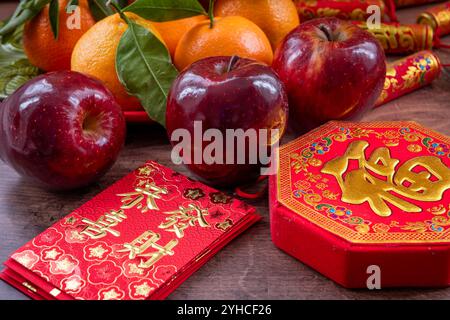 Gros plan d'une assiette de mandarines et de pommes rouges. Décorations lunaires du nouvel an et paquets rouges avec bonne fortune, santé, mots de richesse sur eux. A Chines Banque D'Images