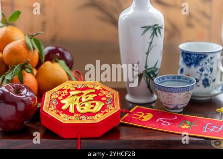 Gros plan sur la bonne fortune et la sécurité des décorations du nouvel an chinois, une bouteille de vin avec des tasses et une assiette de mandarines et de pommes rouges Un nouvel an lunaire Banque D'Images