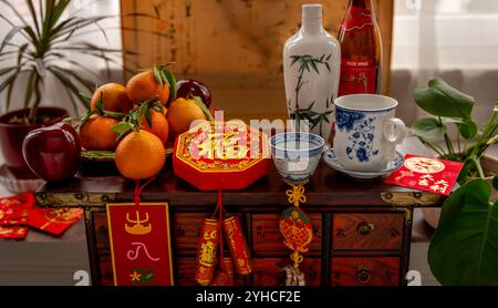 Une bouteille de vin et des tasses. Une assiette de fruits et des décorations du nouvel an chinois de bonne fortune, et des paquets rouges sur un coffre en bois traditionnel. Une nouveauté lunaire Banque D'Images