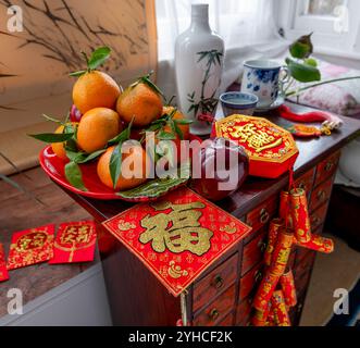 Un concept de nouvel an chinois avec une bouteille de vin et des tasses. Une assiette de fruits, des décorations du nouvel an chinois de bonne fortune, et des paquets rouges sur un traditi Banque D'Images