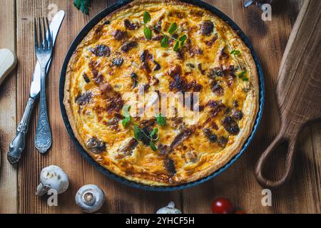 Quiche ou tarte avec de la viande, du poulet et des champignons sur une table en bois avec couverts, herbes et tomates cerises. Photo de haute qualité Banque D'Images