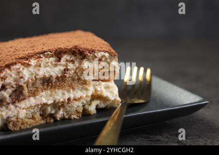 Morceau de savoureux tiramisu et fourchette sur la table noire, gros plan Banque D'Images