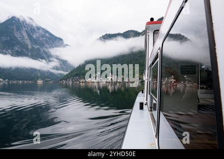 Vue de réflexion de fenêtre de ferry du célèbre village pittoresque de Hallstatt et des montagnes nuageuses, Gmunden, Autriche Banque D'Images
