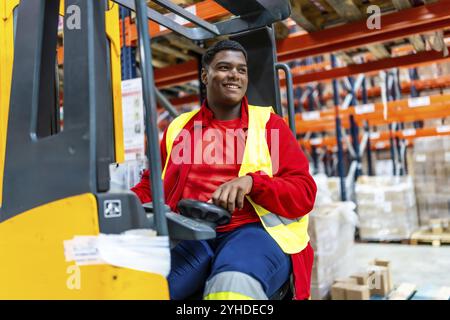 Travailleur latin souriant assis et conduisant un chariot élévateur dans un entrepôt de distribution Banque D'Images