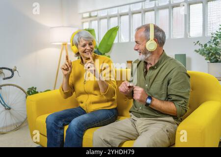 Heureux couple senior écoutant de la musique et dansant assis ensemble sur le canapé Banque D'Images