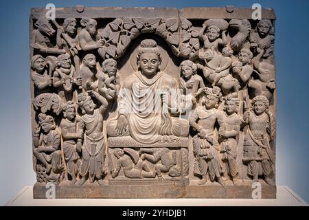 Gandhara Schist relief Buddha Enlightenment Freer Gallery Washington DC // WASHINGTON DC — Un panneau en relief de schiste de l'ancien Gandhara représente l'illumination du Bouddha, le montrant en méditation tandis que l'armée des démons de Mara tente de perturber sa concentration. Créé sous la dynastie Kushan (fin du IIe siècle - début du IIIe siècle de notre ère), ce panneau représente le Bouddha avec un geste touchant la terre (bhumisparsha mudra) symbolisant son triomphe sur la mort et le désir. La scène contraste la symétrie sereine du Bouddha avec les formes déformées des démons de Mara. Ce relief fait partie du texte de la Freer Gallery of Art Banque D'Images