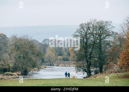 Deux personnes marchant le long des rives de la rivière Wharfe à Bolton Abbey près de Skipton dans le parc national des Yorkshire Dales par un jour nuageux d'automne. Banque D'Images