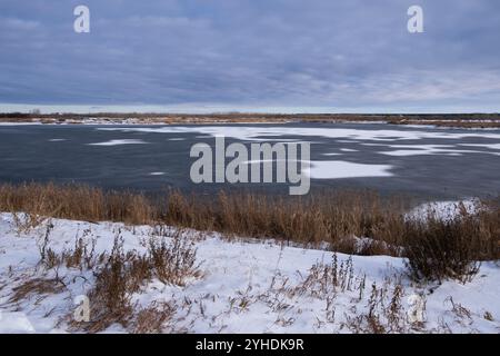 Paysage d'hiver avec lac gelé et herbe sèche sur le rivage Banque D'Images