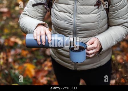 Une touriste verse une boisson chaude du thermos dans une tasse de voyage. Rafraîchissement pendant la randonnée dans la forêt d'automne Banque D'Images