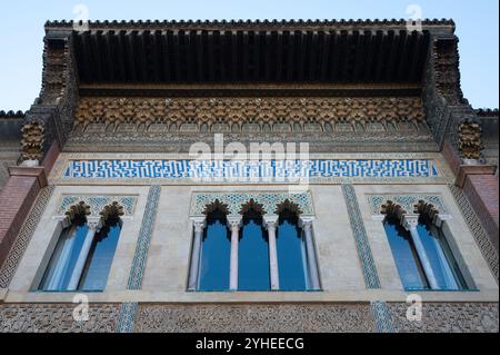 Le sommet d'un magnifique bâtiment historique à Séville, orné de carreaux colorés, de boiseries complexes et de trois élégantes fenêtres encadrées par des colonnes Banque D'Images