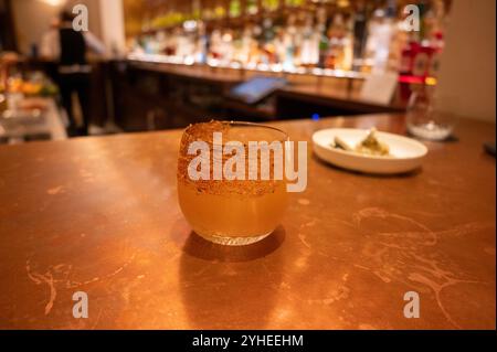 Une margarita épicée avec un bord de tajin se trouve sur un comptoir de bar, offrant un goût audacieux et rafraîchissant, avec des bouteilles de liqueur floues en arrière-plan Banque D'Images