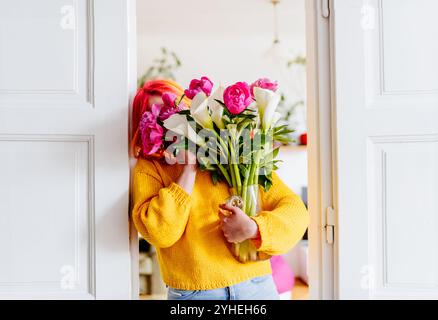 Femme tenant un bouquet coloré dans un pull jaune vif près de la porte Banque D'Images