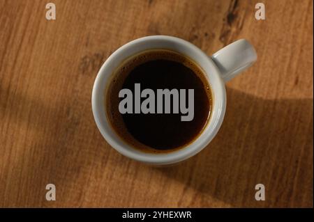 Une tasse de café noir fumant se trouve sur une table en bois rustique, prélassant dans la lumière chaude du soleil matinal. Banque D'Images