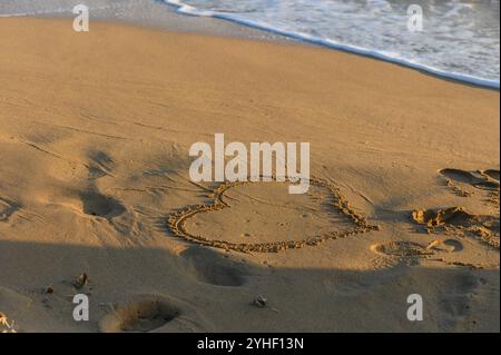 Un cœur sablonneux tourbillonne doucement sur le rivage tandis que les vagues embrassent doucement la plage au crépuscule. Banque D'Images