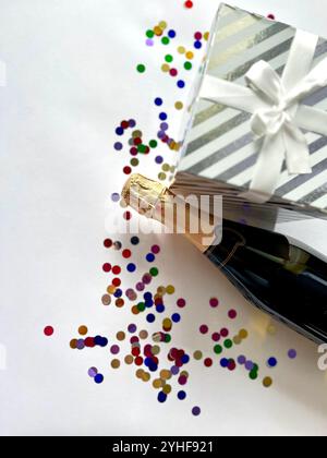 Bouteille de champagne avec paillettes colorées, confettis et espace de boîte cadeau pour le texte sur fond coloré, vue de dessus. Banque D'Images