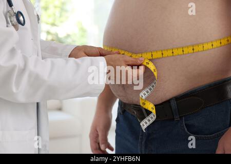 Nutritionniste mesurant la taille de l'homme en surpoids avec du ruban adhésif en clinique, gros plan Banque D'Images