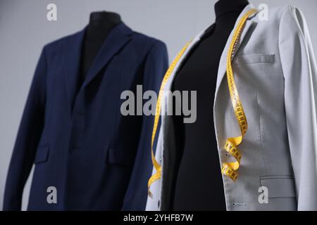 Mannequins avec vestes et ruban à mesurer sur fond gris, gros plan Banque D'Images