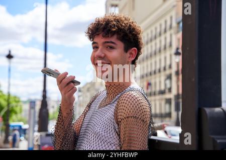 Un homme sourit avec un téléphone portable à la main. Il porte un débardeur et un T-shirt en résille. Banque D'Images