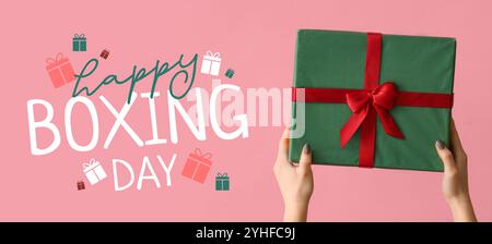 Mains tenant le cadeau de Noël sur fond rose. Bannière pour le lendemain de Noël Banque D'Images