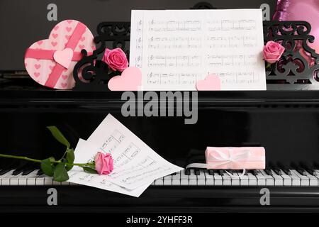 Piano avec feuilles de notes, roses roses et cadeaux pour la Saint-Valentin sur fond sombre Banque D'Images