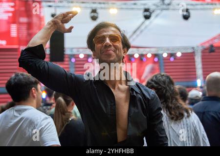 Homme indien en chemise noire et lunettes de soleil célébrant lors d'un concert, levant le bras et souriant. Banque D'Images