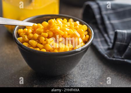 Maïs sucré en conserve dans un bol sur une table de cuisine noire. Banque D'Images