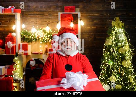 Joyeux Noël et bonne année. Surpris le Père Noël avec un cadeau de Noël. Homme barbu en costume de Père Noël et chapeau de Père Noël avec cadeau de Noël pour K. Banque D'Images