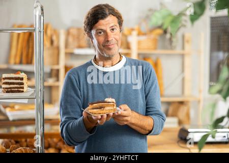 Heureux gars d'âge moyen tenant la pâtisserie sur une assiette de papier dans la boulangerie Banque D'Images