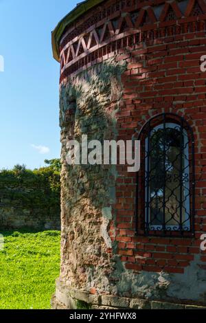 Tour en briques altérées avec une fenêtre voûtée et des barres de fer, présentant des détails architecturaux rustiques et historiques sous la lumière du soleil Banque D'Images