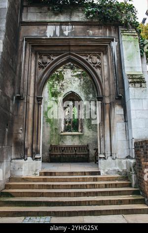 Une ancienne arche en pierre altérée avec un banc en dessous et une fenêtre partiellement envahie, mettant en valeur la beauté de l'architecture abandonnée. Banque D'Images