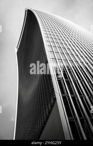 Une photo en noir et blanc de l'extérieur courbé et métallique d'un gratte-ciel moderne, mettant en valeur les lignes géométriques et le motif du bâtiment. Banque D'Images