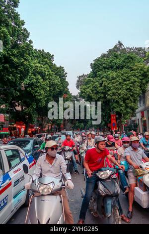 Une scène de rue animée à Hanoi, au Vietnam, montrant un trafic dense avec des voitures et des motos se déplaçant le long de routes bordées d'arbres. Banque D'Images