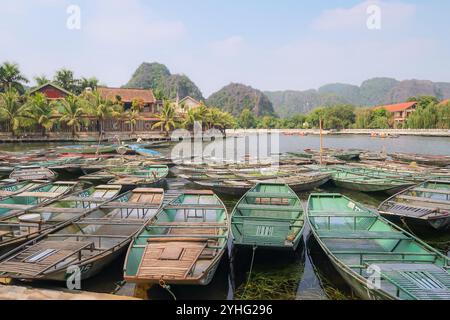 Bateaux verts traditionnels à un quai vietnamien, prêts pour les touristes. Vue panoramique sur la verdure luxuriante, les montagnes et les eaux calmes dans un cadre tropical. Banque D'Images