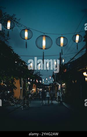 Rue nocturne à Hoi an, Vietnam, avec des lanternes illuminées suspendues au-dessus des piétons, créant une atmosphère magique dans la ville antique. Banque D'Images