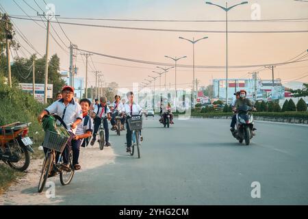 Groupe d'écoliers à vélo et en scooter le long d'une rue de la ville, capturant un trajet animé au Vietnam. Banque D'Images