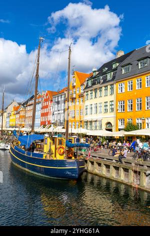 Scène de divertissement et de restaurant à Copenhague à côté du canal dans le quartier de Nyhavn avec des bateaux le long du canal et les gens appréciant un déjeuner au restaurant Banque D'Images