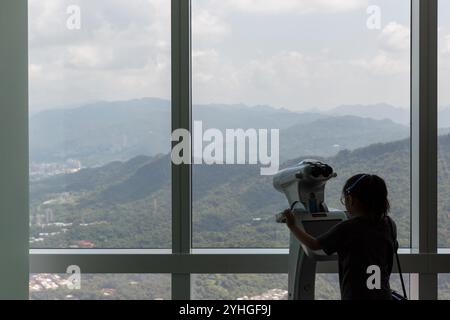 Un enfant utilisant l'une des jumelles sécurisées à la terrasse d'observation de Taipei 101. Banque D'Images