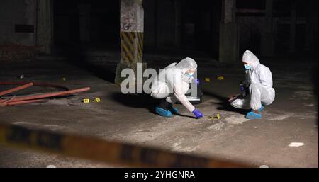 Scène de crime, personnes et criminalistique la nuit avec écouvillon, preuves ou indices d'ADN dans un entrepôt abandonné. L'équipe CSI, la poursuite Hazmat ou l'enquête Banque D'Images