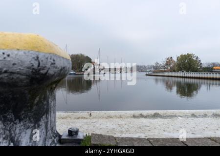 Une vue calme sur le port de Ueckermünde en novembre, avec un gros plan d'une borne d'amarrage au premier plan et des eaux calmes. Banque D'Images