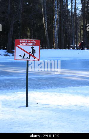 Interdisant le panneau routier 'dangereux! Restez hors de la glace » avec une inscription en russe et un symbole petit homme près d'une rivière couverte d'orien vertical de glace Banque D'Images