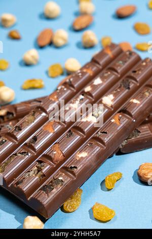 Barres de chocolat noisettes parmi les noix dispersées et les raisins secs sur un fond bleu. Banque D'Images