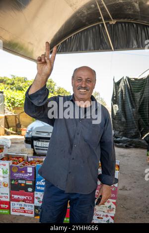 Tulkarm, Palestine – 18 juillet 2023 : Happy Arab homme entrepreneur se tient dans un hangar à la campagne et fait le signe de la paix avec sa main droite Hig Banque D'Images