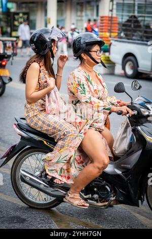 Deux filles thaïlandaises assises sur une moto ou un scooter font leur chemin le long de soi Buakhao, Pattaya City, Thaïlande. Banque D'Images