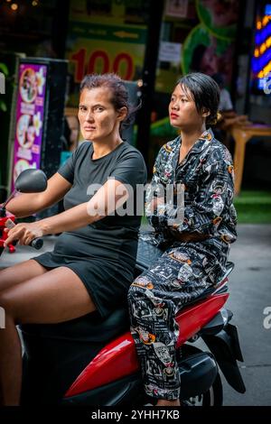 Deux filles thaïlandaises assises sur une moto ou un scooter font leur chemin le long de soi Buakhao, Pattaya City, Thaïlande. Banque D'Images