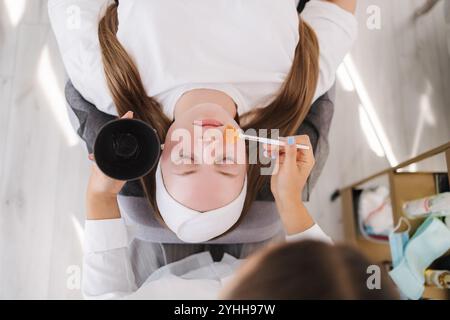 Vue de dessus du client se détend sur un lit de traitement avec un masque de soin appliqué, soulignant l'expérience calme et rajeunissante du spa. Banque D'Images