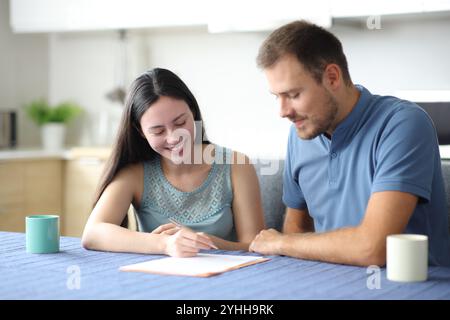 Heureux colocataires interraciaux ou couple signant contrat dans la cuisine à la maison Banque D'Images