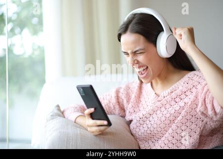 Femme excitée regardant les médias sur téléphone intelligent célébrant le succès à la maison Banque D'Images