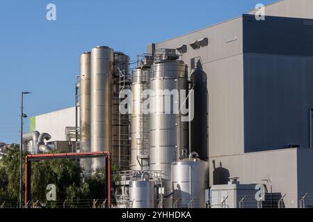 Les silos métalliques et les tuyauteries complexes se dressent face à un ciel bleu clair dans une usine de traitement industriel moderne Banque D'Images