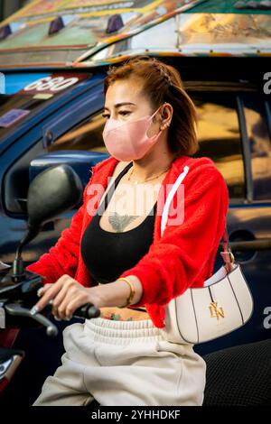 Une jeune dame thaïlandaise assise sur une moto ou un scooter fait son chemin le long de soi Buakhao, Pattaya City, Thaïlande. Banque D'Images