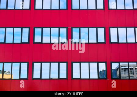 Bâtiment de couleur rouge profond avec plusieurs fenêtres en miroir, reflets du ciel et des nuages Banque D'Images